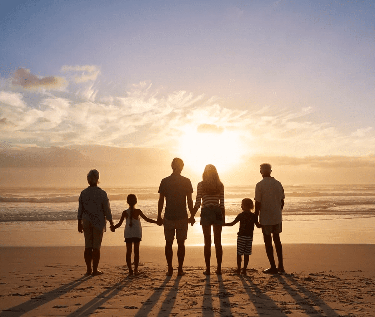 Family holding hands, watching beach sunset.